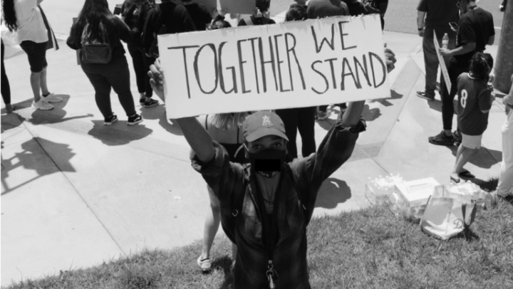A Black person holding a sign over their head saying TOGETHER WE STAND